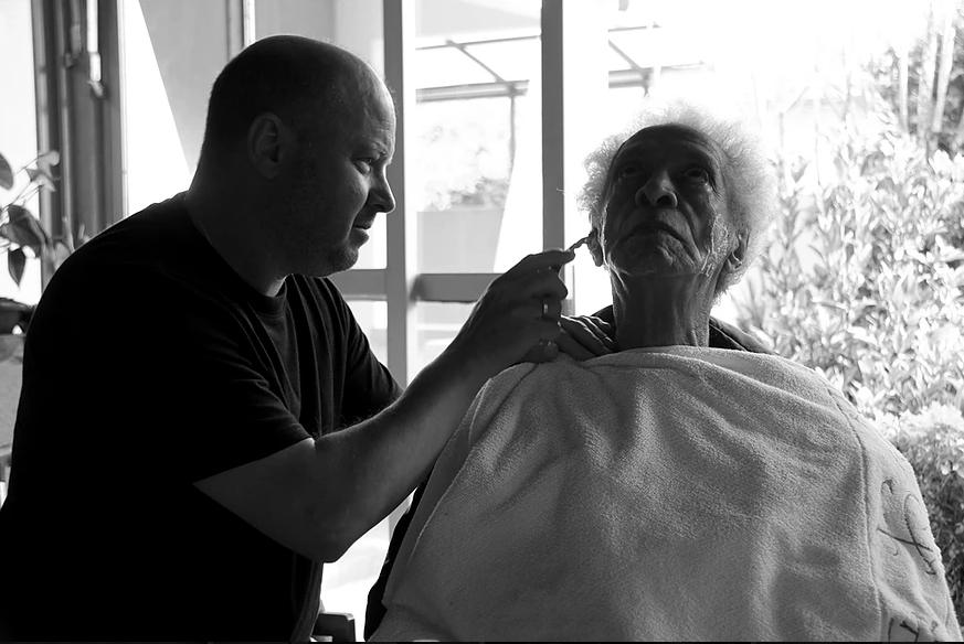 o produtor Virgílio Milléo barbeia Waltel Branco em cena do documentário. | Divulgação/