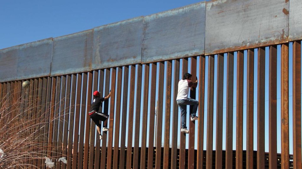 Garotos tentam atravessar uma barreira erguida na fronteira entre México e EUA | Herika Martinez/AFP