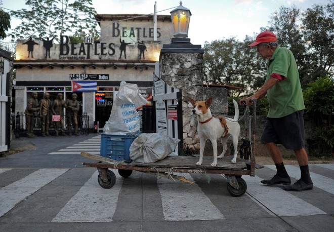 Homem passeia com seu cachorro; ao fundo, a fachada do Beatles Bar, em Varadero. | Yamil Lage/AFP