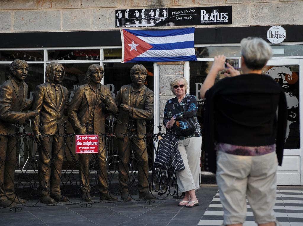 Turista posa ao lado de esculturas dos Beatles em frente de bar temático em Varadero, província de Matanza. | Yamil Lage/AFP