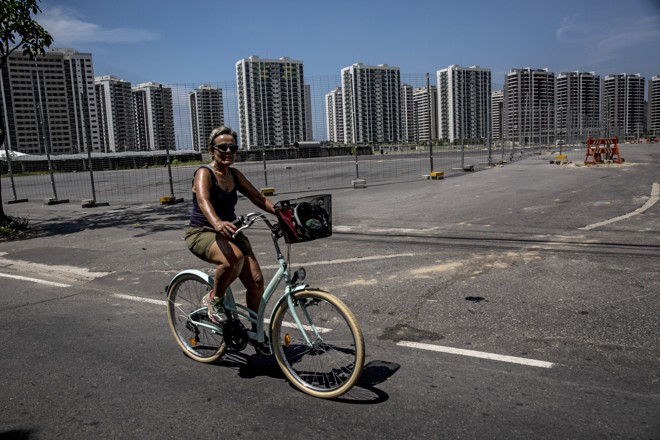 Moradora anda de bicicleta nas proximidades da Vila dos Atletas, que foi concebida como empreendimento imobiliário. E fracassou em vendas | DADO GALDIERI/NYT