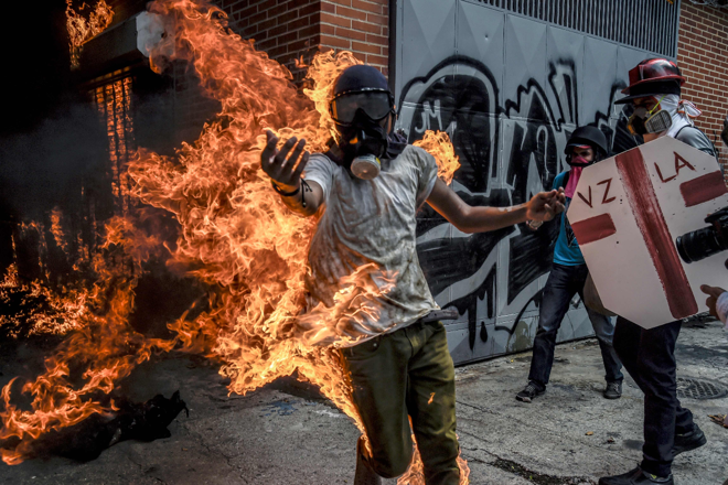 Esta foto, feita no dia 03 de maio, mostra o manifestante anti-Maduro Victor Salazar em chamas depois que o tanque de gasolina de uma motocicleta da polícia explodiu durante os protestos em Caracas. Do hospital, com 70% do corpo queimado, Salazar mandou uma mensagem aos venezuelanos em vídeo: “Vão para as ruas, não por mim, mas pela Venezuela." | JUAN BARRETO/AFP