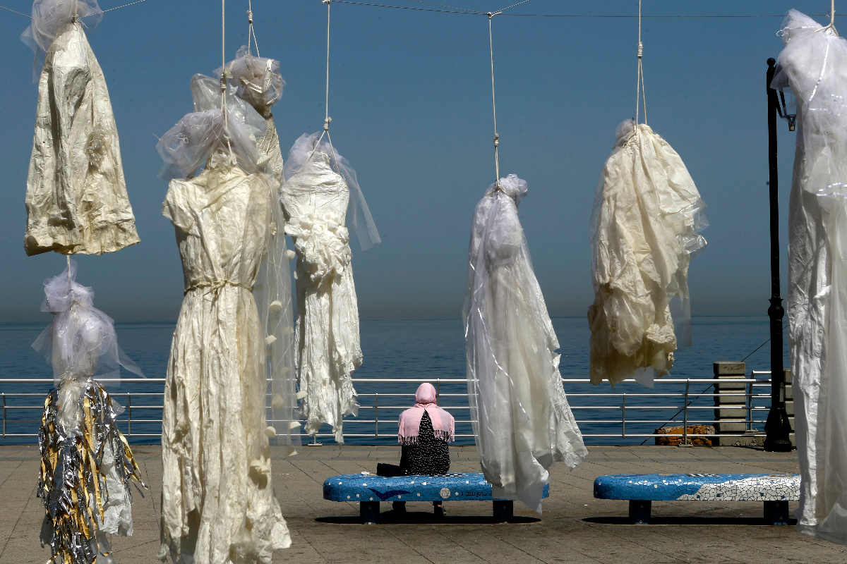 Mulher senta-se em um banco perto de uma instalação da artista libanesa Mireille Honein, com vários vestidos de noiva amarrados, denunciando o artigo do código penal libanês que permite aos estupradores casarem com suas vítimas para escaparem à prisão. A lei é comum em vários países do Oriente Médio, como a Jordânia | PATRICK BAZAFP