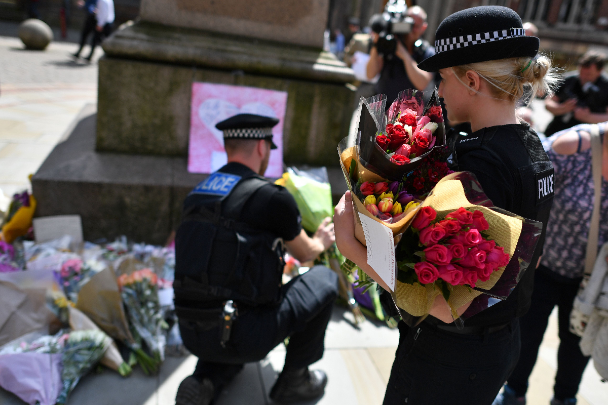 Policiais mudam de lugar as flores colocadas na Praça Santa Ana, em homenagem às vítimas do atentado desta segunda-feira (22) | BEN STANSALL/AFP