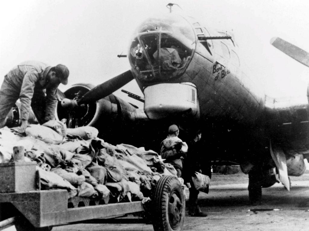 Trabalhadores carregam alimentos em avião bombardeiro dos Estados Unidos durante operação da Segunda Guerra Mundial. Avião lançou comida ao invés de bombas para holandeses.