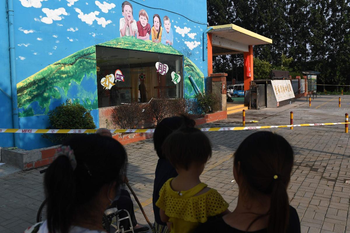 Moradores da região observam do lado de fora do jardim de infância. Local foi isolado pela polícia | GREG BAKERAFP