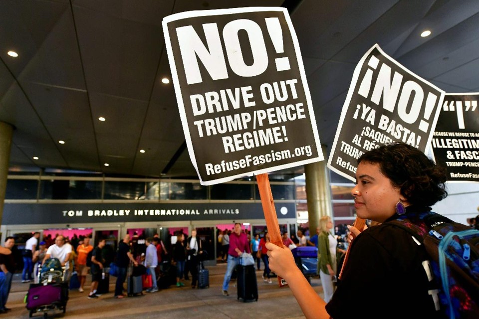 Ativista segura cartazes contra a política de imigração do governo Trump no setor de desembarque do aeroporto internacional de Los Angeles. | FREDERIC J. BROWN/AFP