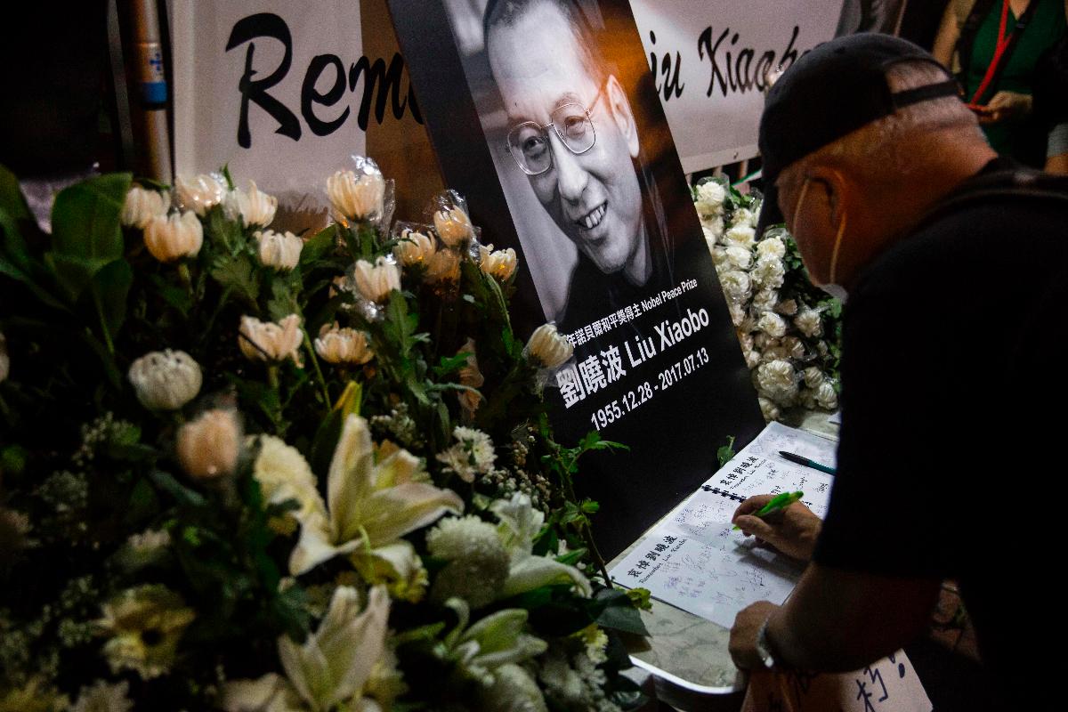 Homem escreve mensagem para o Prêmio Nobel da Paz de 2010 Lu Xiaobo no memorial improvisado em frente a um escritório do governo chinês em Hong Kong | ISAAC LAWRENCE/AFP