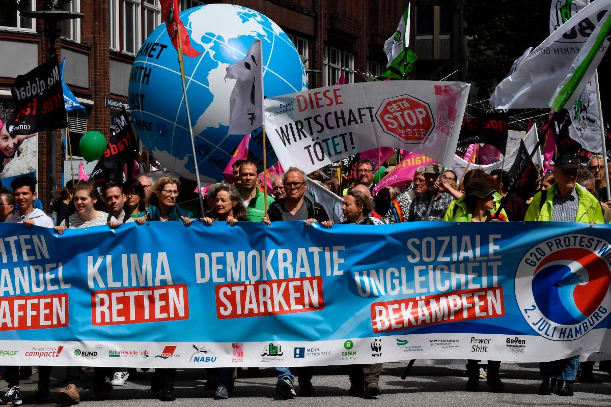 Manifestantes marcham atrás de uma bandeira anti G-20 em um ato convocado por várias ONGs em Hamburgo, Alemanha | JOHN MACDOUGALLAFP