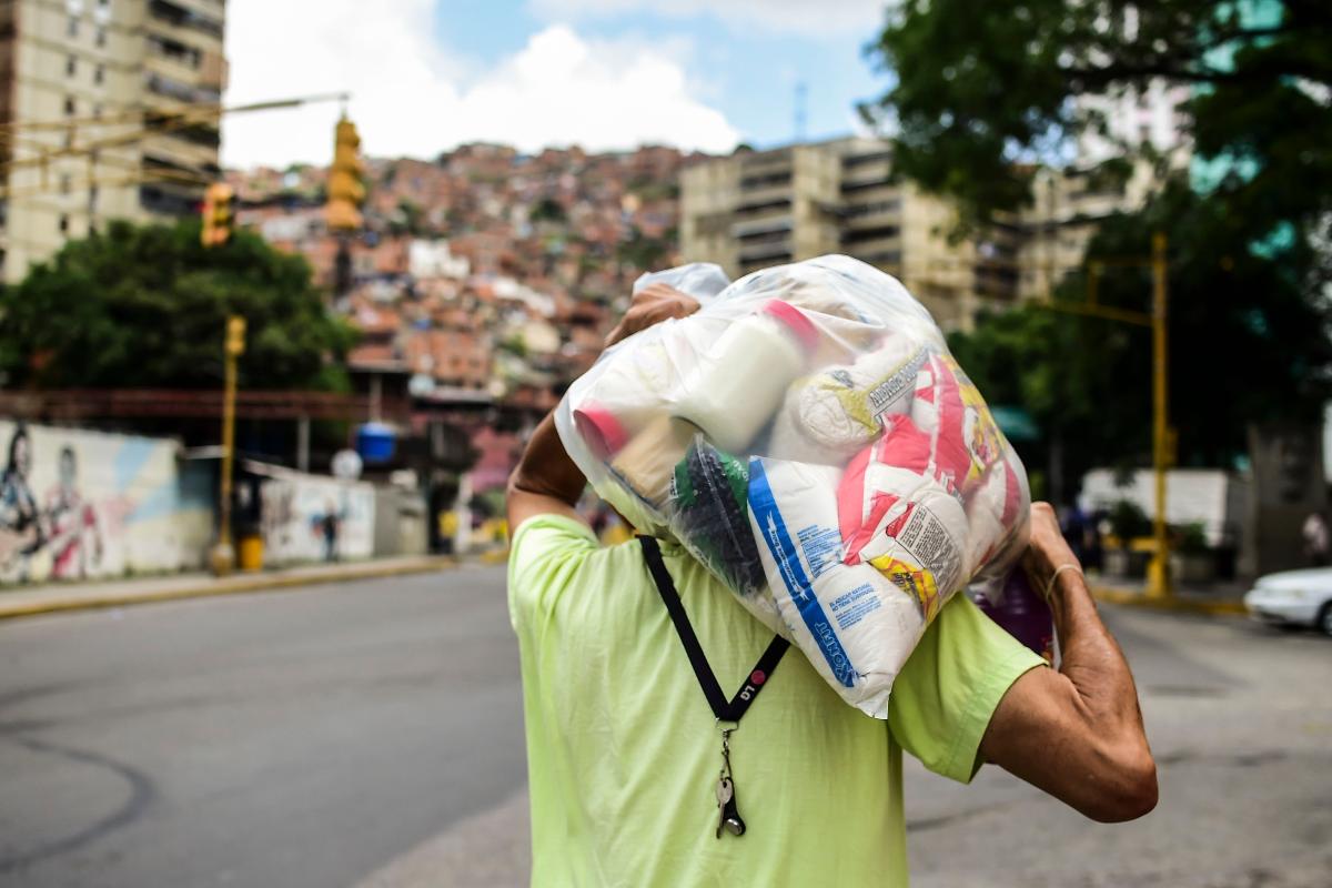 Homem carrega alimentos, ao sair de um dos centros de distribuição denominados CLAP (Comitês Locais de Fornecimento e Produção), dirigidos por líderes comunitários, em Caracas, em 16 de agosto de 2017. Os pacotes de alimentos subsidiados pelo estado (cerca de US$ 4) contêm ingredientes básicos como arroz, farinha, macarrão, feijão, óleo, açúcar e leite e são distribuídos a cada mês e meio, não sendo suficientes em meio a uma crise em que a escassez de gêneros alimentícios, produtos de higiene e remédios é comum | RONALDO SCHEMIDT/
AFP