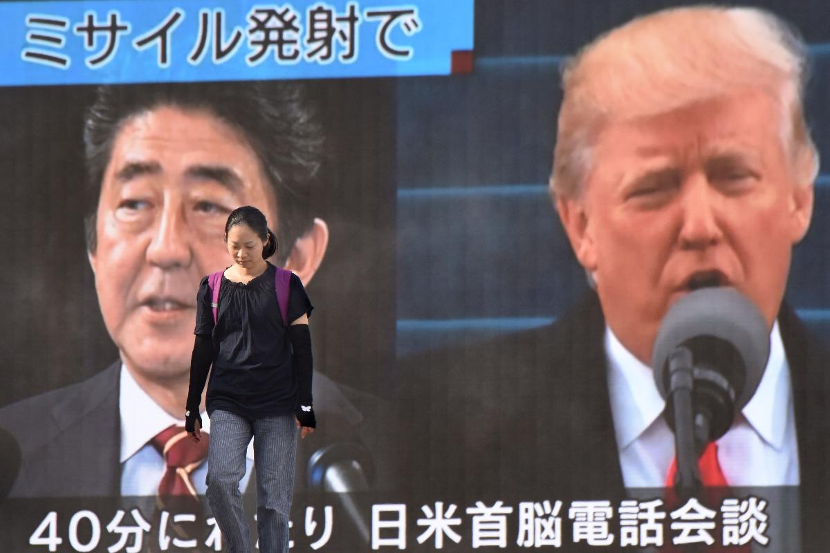 Mulher caminha em frente à display com imagens do premiê japonês, Shinzo Abe, e o presidente dos Estados Unidos, Donald Trump, nesta terça-feira, no Japão; ambos são a favor de aumentar a pressão para que a Coreia do Norte interrompa programa nuclear | KAZUHIRO NOGI/
AFP
