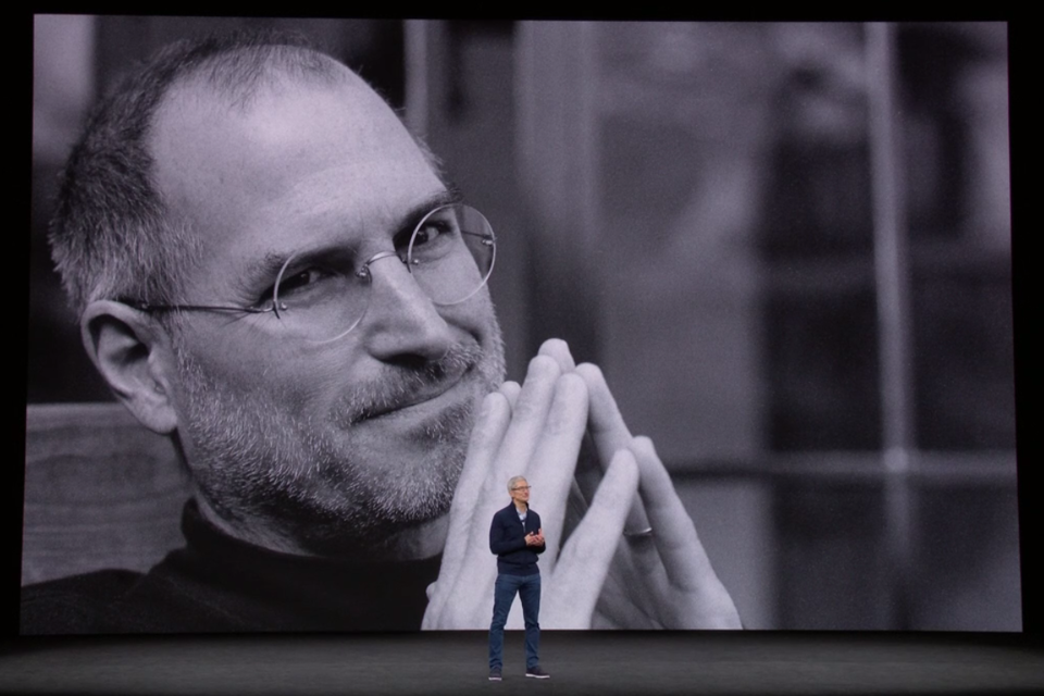 No centro, Tim Cook, atual CEO da Apple, e na imagem ao fundo Steve Jobs, fundador da Apple. | Reprodução/Apple Event