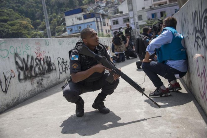 Polícias e jornalistas se protegem durante operação para combater traficantes de drogas fortemente armados na favela da Rocinha, no Rio de Janeiro, em 22 de setembro de 2017. | MAURO PIMENTEL/
AFP