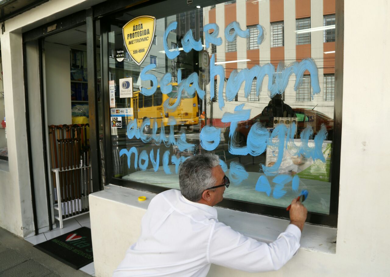 Rogério Bonini escreve a frase na vitrine da Vita’s: objetivo é que pedestres e passageiros leiam e se conscientizem. | Aniele Nascimento /Gazeta do Povo