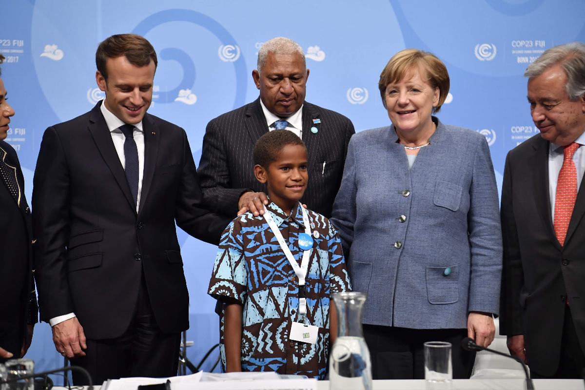 Frank Bainimarama (centro), primeiro-ministro das Fiji e presidente da COP 23, o presidente francês Emmanuel Macron (à esquerda), a chanceler alemã Angela Merkel e o secretário-geral da ONU Antonio Guterres (à direita) junto com um jovem jovem fijiano que discursou antes da sessão de abertura na conferência da ONU sobre mudanças climáticas (COP23) em 15 de novembro de 2017 em Bonn, na Alemanha. | JOHN MACDOUGALL/AFP