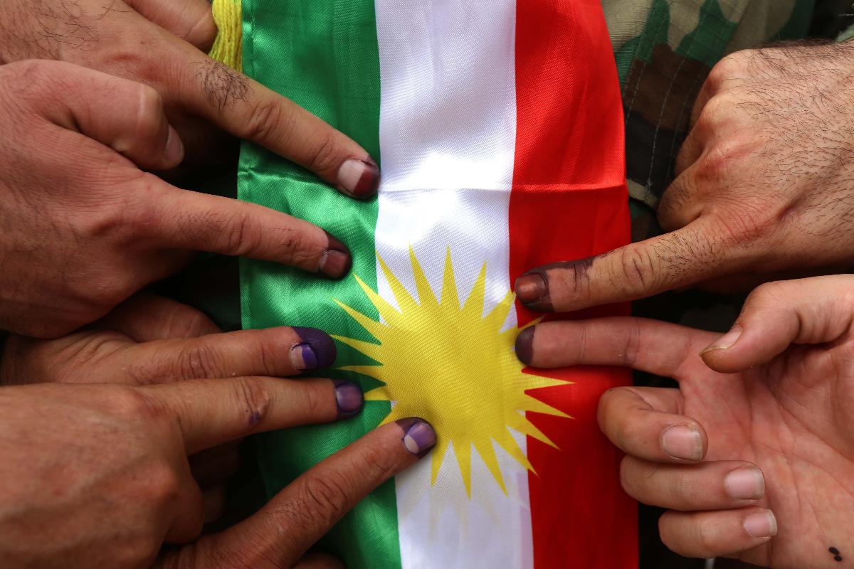 Dedos manchados de tinta apontam para a bandeira curda após o referendo realizado em 25 de setembro | SAFIN HAMED/AFP
