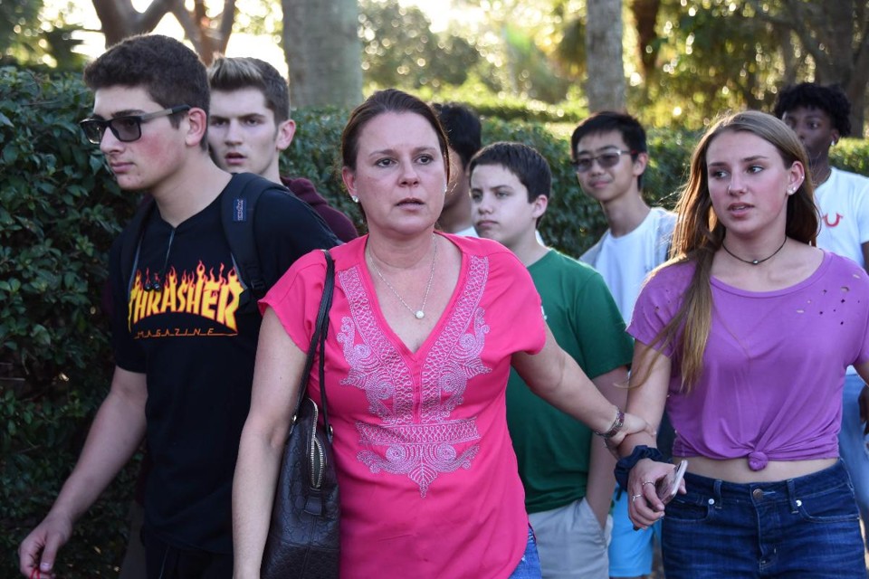 Estudantes e adultos saem da escola secundária Marjory Stoneman Douglas  em Parkland, Flórida, cidade a cerca de 50 quilômetros a norte de Miami, em 14 de fevereiro de 2018. Dezessete pessoas morreram quando um ex-aluno de 19 anos disparou com um rifle semi-automático, disse o xerife local, chamando a cena de "horrível". O xerife do condado de Broward, Steve Israel, disse que as vítimas eram uma mistura de estudantes e adultos, embora não pudesse confirmar se os adultos eram professores. | MICHELE EVE SANDBERG/AFP