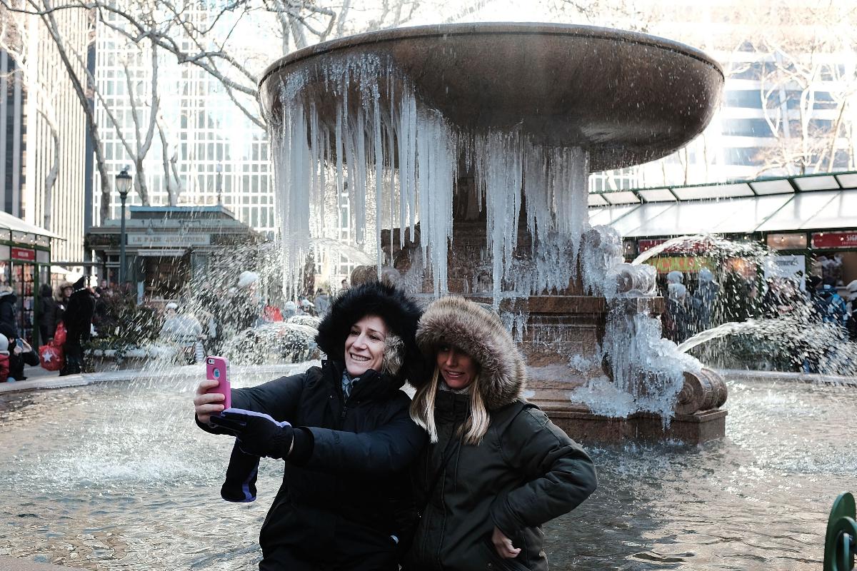 Duas mulheres fazem uma selfie em frente a uma fonte congelada no parque Bryant, em Manhattan, Nova York, em 27 de dezembro. | SPENCER PLATTAFP