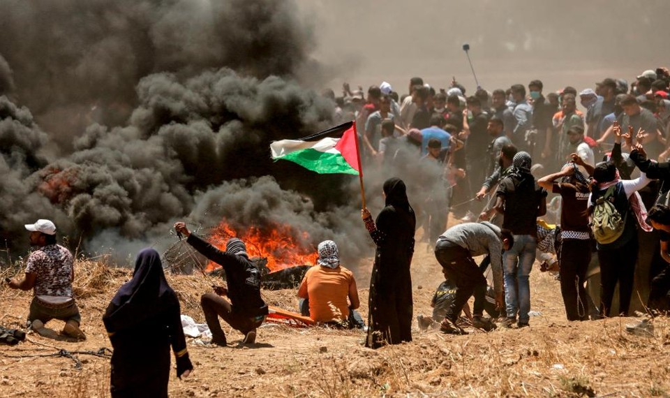 Mulher palestina segura bandeira nacional durante confronto entre forças israelenses e palestinos na fronteira entre Faixa de Gaza e Israel | MAHMUD HAMS/AFP