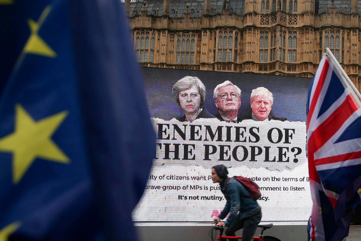 Manifestantes anti-Brexit e pró-UE acenam bandeiras da União Européia e do Reino Unidos com um outdoor que representa a primeira-ministra da Grã-Bretanha, Theresa May, o Secretário de Estado da Grã-Bretanha para a Saída da União Européia (Ministro Brexit) David Davis e o Ministro dos Negócios Estrangeiros da Grã-Bretanha, Boris Johnson, no centro de Londres, em 13 de dezembro de 2017, enquanto os deputados debatiam o projeto de retirada da UE. | DANIEL LEAL-OLIVAS/AFP