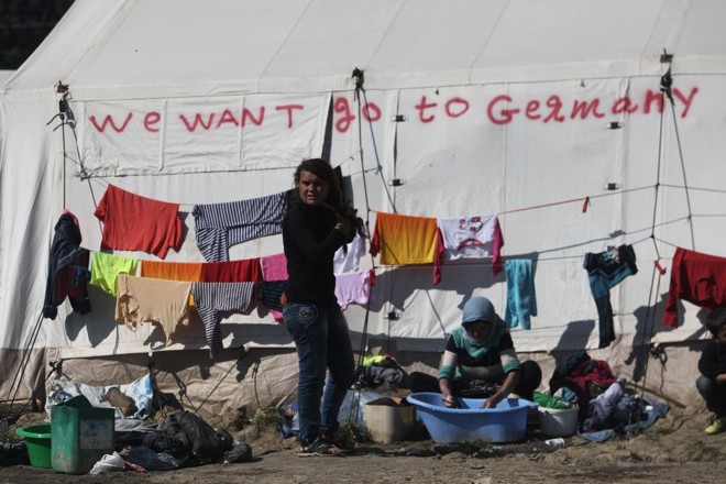 Imigrantes no campo de refugiados na fronteira entra a Grécia e Macedônia em frente a uma tenda que diz “Nós queremos ir para a Alemanha”, em março de 2016. | SAKIS MITROLIDISAFP