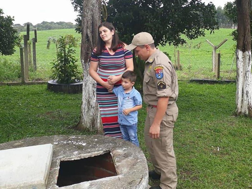 Soldado José Geovane de Assis com o filho resgatado e a esposa, em frente ao local do acidente. | Divulgação/Corpo de Bombeiros