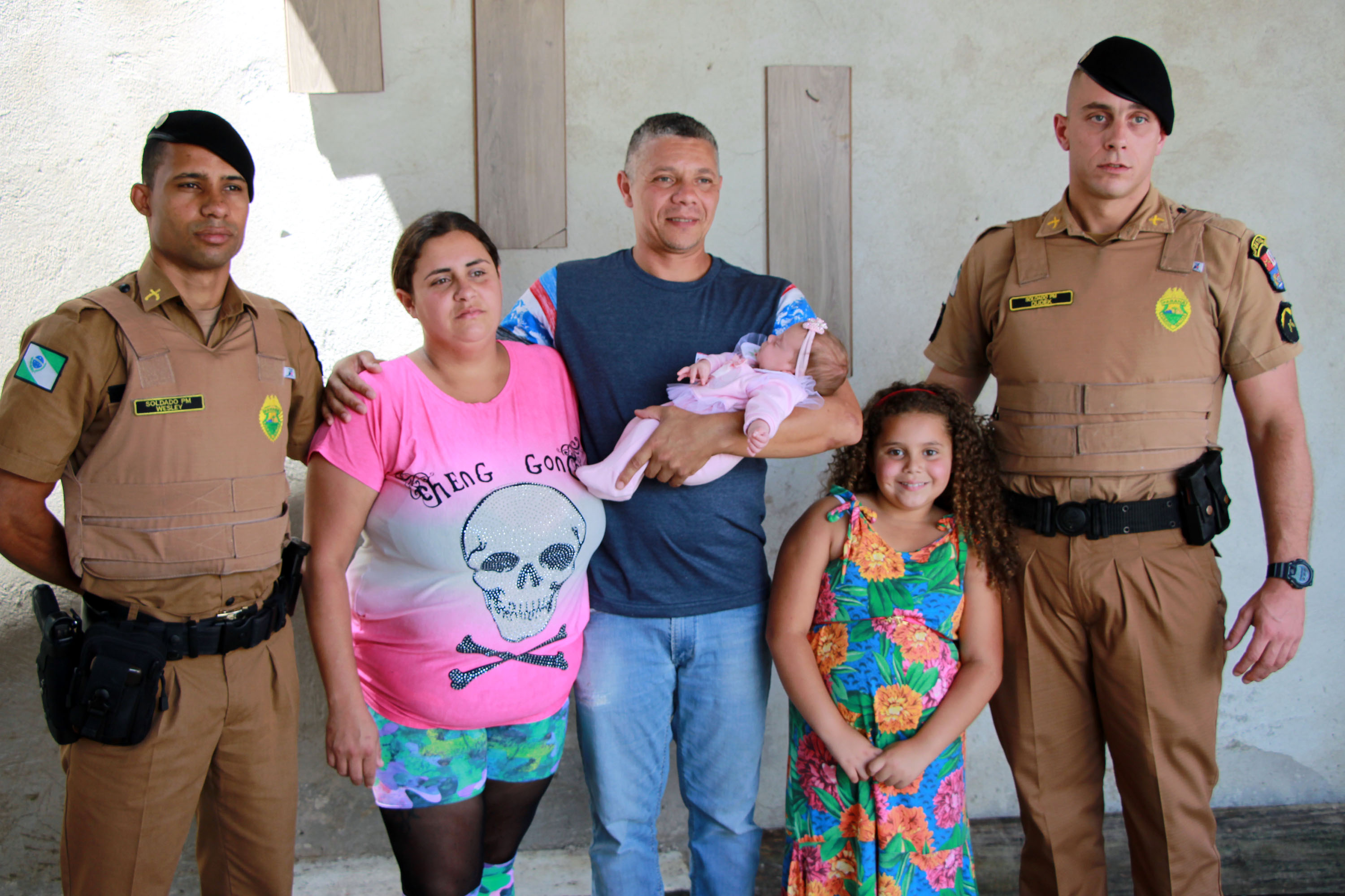 Aurora com os pais e os policiais que a salvaram: à esquerda Wesley Alves Soares, que ajudou no parto,  e à direita Walter Dudek Filho, que a salvou de engasgamento. | Soldado Adilson Voinaski Afonso/Polícia Militar