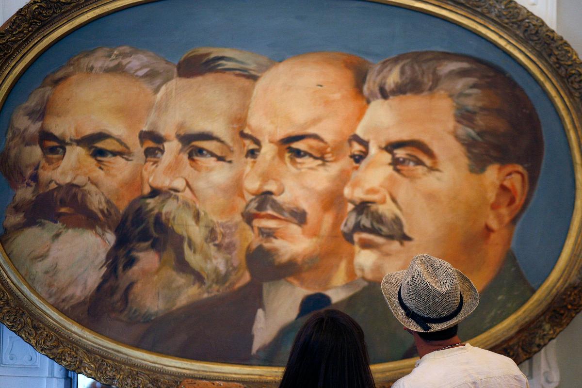 Visitantes olham para pintura parte da exposição "Arte totalitária" na Galeria Nacional de Arte, em Sofia, Bulgária, 9 de julho de 2009. Os retratos na pintura são autores de "O Manifesto Comunista", Karl Marx (à esquerda) e Friedrich Engels, o fundador do Estado soviético Vladimir Lenin e do falecido ditador soviético Joseph Stalin. | SN/WYSTOYAN NENOV