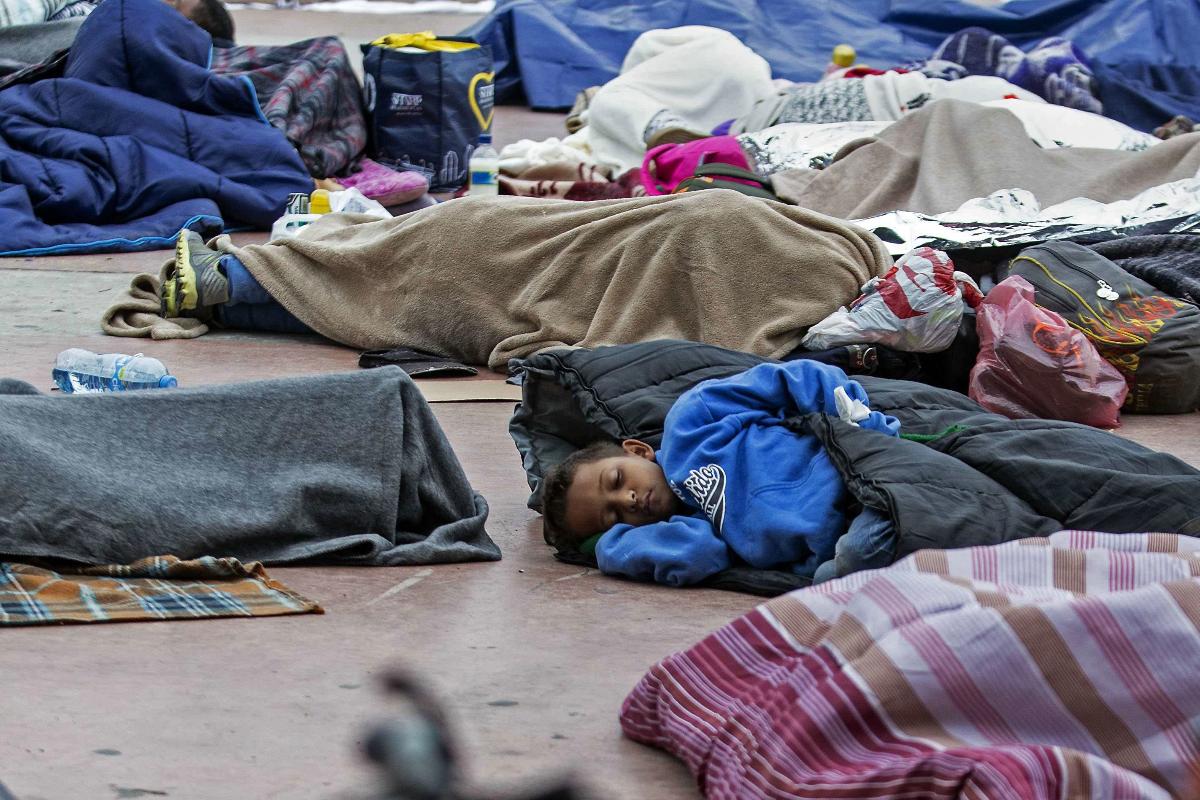 Migrantes da América Central, que viajaram de caravana para os EUA, dormem em frente ao porto "El Chaparral" e aguardam para serem recebidos pelas autoridades norte-americanas | GUILLERMO ARIAS/AFP