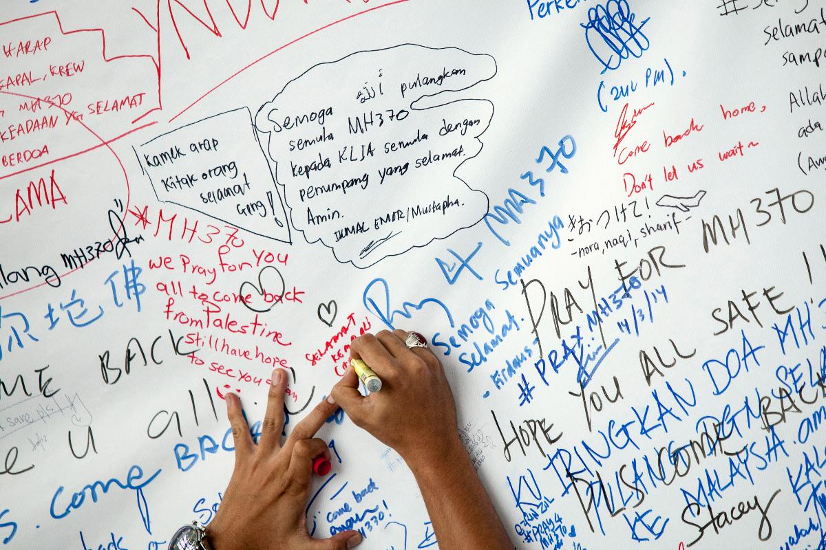 Homem escreve mensagem em cartaz sobre o avião desaparecido da Malaysia Airlines, no aeroporto de Kuala Lumpur | Charles Pertwee/Bloomberg
