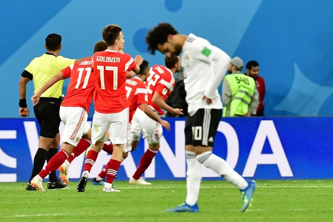 Egípcio Salah lamenta enquanto atletas da Rússia celebram um dos três gols do time da casa | GIUSEPPE CACACE/AFP