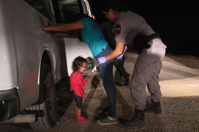 Uma menina hondurenha de dois anos de idade chora enquanto sua mãe é revistada e detida perto da fronteira EUA-México em 12 de junho de 2018 em McAllen, Texas | JOHN MOOREAFP