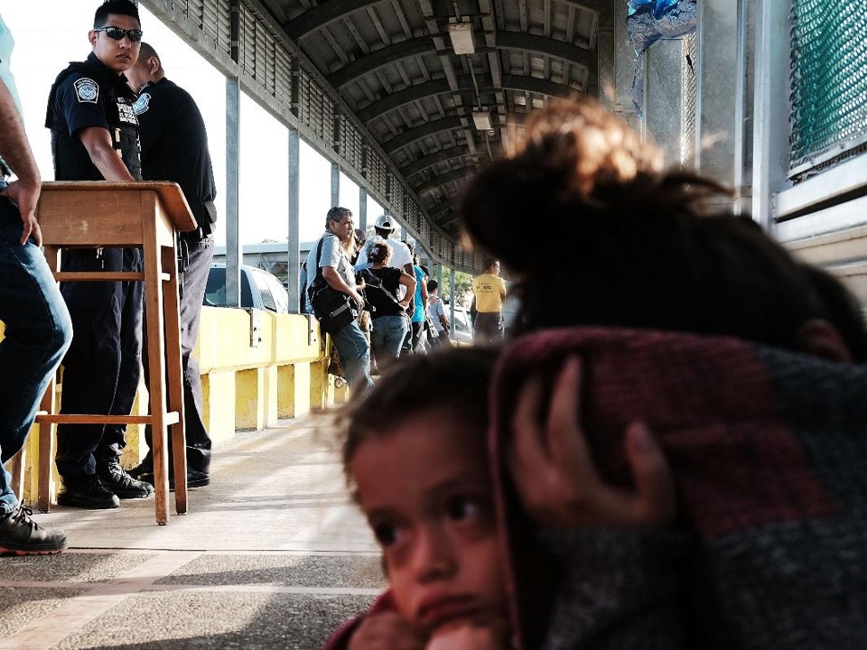 Uma criança hondurenha e sua mãe esperam em uma fila ao longo da ponte que liga o México aos EUA, em 25 de junho de 2018 em Brownsville, Texas | SPENCER PLATTAFP