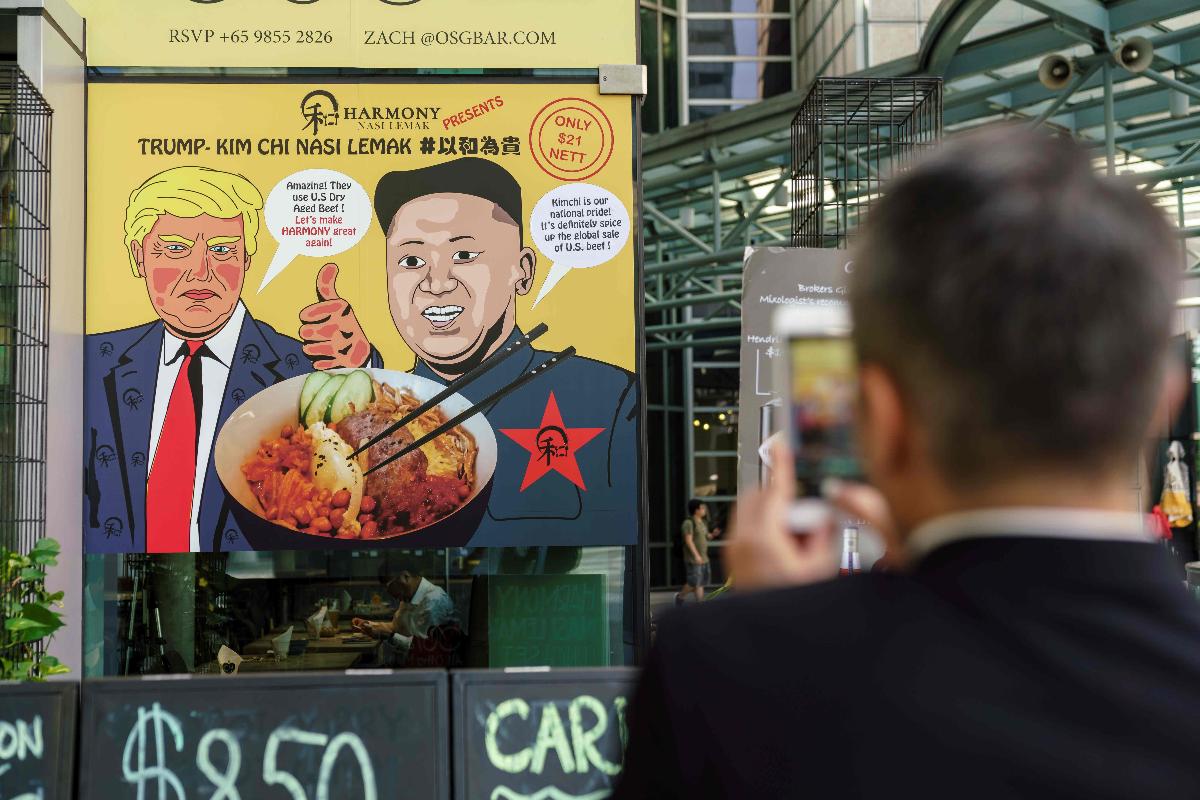 Um homem fotografa um cartaz oferecendo um "Trump-Kim Chi" nasi lemak, um popular prato local, em um restaurante em Cingapura | NICHOLAS YEOAFP