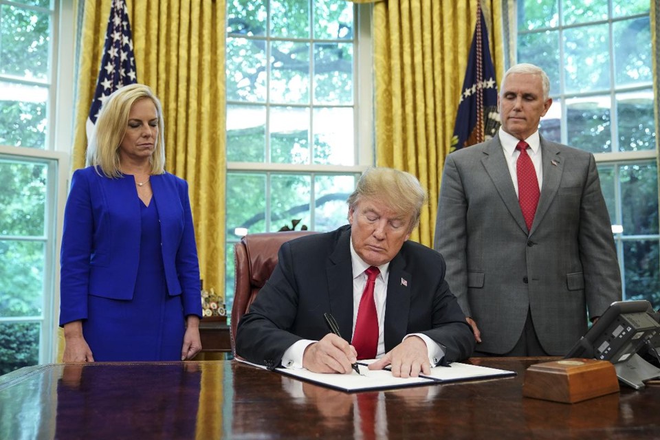 Presidente dos EUA, Donald Trump, assina ordem executiva ao lado da secretária de Segurança Interna, Kirstjen Nielsen, e do vice-presidente, Mike Pence | MANDEL NGANAFP