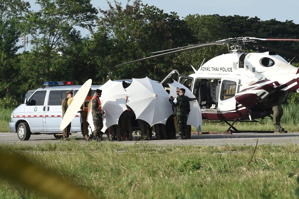 Militares e policiais usam guarda-chuvas para proteger os meninos da luz ao transferi-los da ambulância para o helicóptero | LILLIAN SUWANRUMPHAAFP