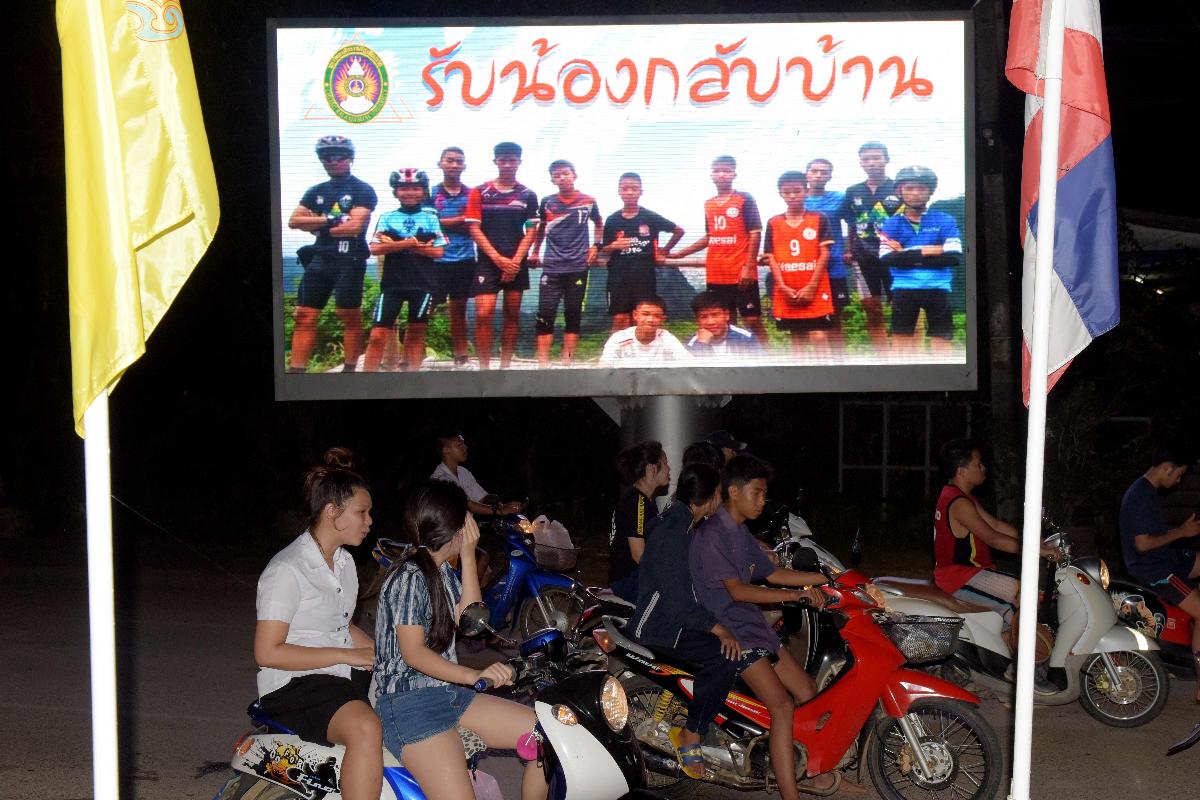 Motoristas passam em um outdoor exibindo uma fotografia do time de futebol infantil tailandês "Wild Boars" e de seu treinador, com uma mensagem de boas-vindas em Chiang Rai, em 10 de julho de 2018, após o resgate. | TANG CHHIN SOTHY/AFP