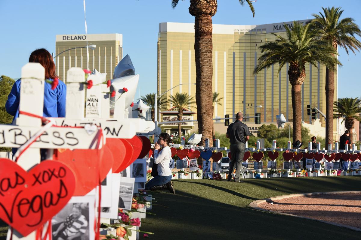 Nesta foto de arquivo, uma mulher reza ao lado de 58 cruzes brancas em homenagem às vítimas do tiroteio em massa de 1º de outubro de 2017. Ao fundo o hotel Mandalay Bay | ROBYN BECKAFP