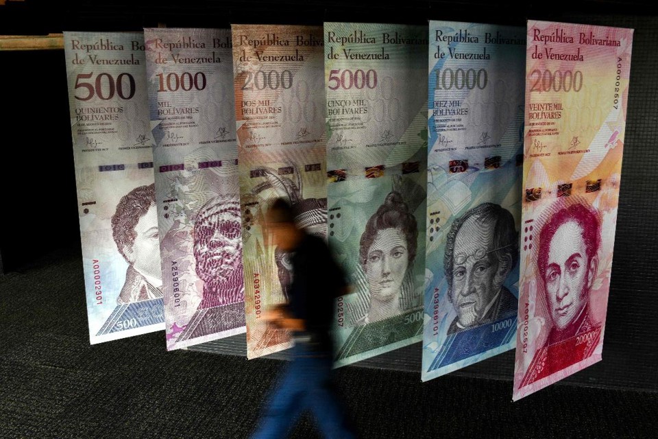 Nesta foto de arquivo tirada em 31 de janeiro de 2018, um homem passa por cartazes representando a moeda da Venezuela, o Bolívar, no Banco Central da Venezuela (BCV) em Caracas | FEDERICO PARRAAFP