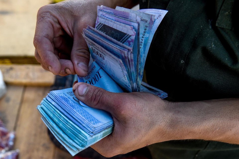 Homem conta notas de 1.000 bolivares (R$ 0,03) para comprar verduras em um mercado na zona metropolitana de Caracas | FEDERICO PARRA/AFP