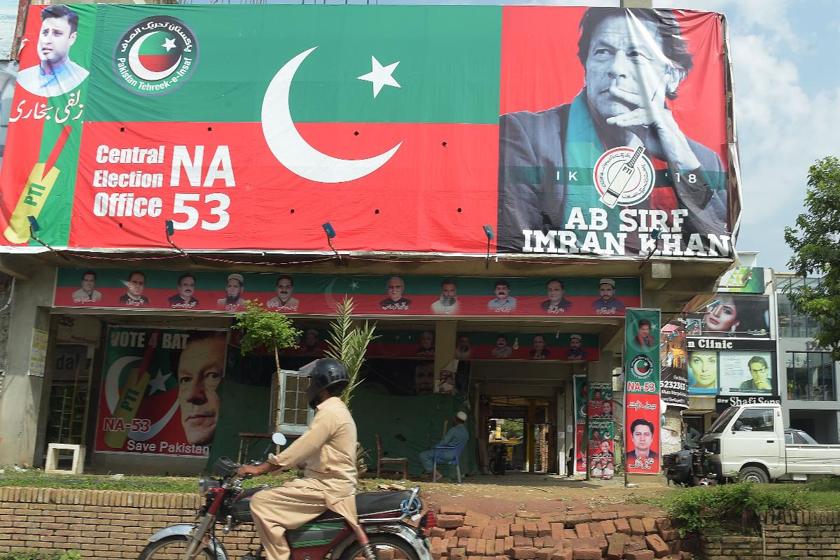 Um motociclista paquistanês passa por um outdoor com uma imagem do político paquistanês Imran Khan, presidente do partido PTI (Movimento pela Justiça), um dia depois da eleição geral em Islamabad, em 26 de julho de 2018 | AAMIR QURESHI/AFP
