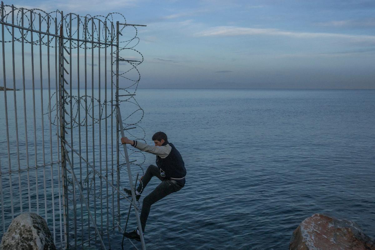 Anas, um imigrante da Argélia, escalando uma cerca ao redor do porto em Mitilene, capital da ilha grega de Lesbos, enquanto tentava entrar escondido em um navio para Atenas, em 4 de março de 2018 | MAURICIO LIMA/NYT