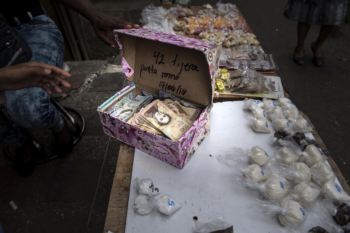 Vendedor de rua abre uma caixa com notas de bolívar em uma banca na favela de Petare, em Caracas | Carlos Becerra/Bloomberg