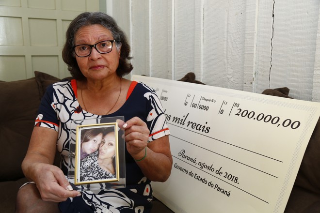 Maria Salete, com o retrato da filha Tatiane e da neta Julia, e o cheque que vai mudar a vida da família. | Aniele Nascimento/Gazeta do Povo