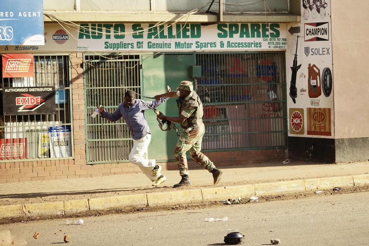 Um soldado zimbabuense bate um homem em uma rua de Harare, capital do Zimbábue, enquanto pessoas protestam devido à suposta fraude na eleição do país | ZINYANGE AUNTONYAFP