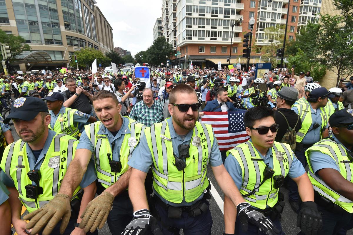Polícia escolta os manifestantes de extrema-direita liderados pelo organizador do 'Unite the Right', Jason Kessler (bandeira), durante um protesto em Lafayette Park, em frente à Casa Branca em 12 de agosto de 2018, em Washington, DC | NICHOLAS KAMM/AFP