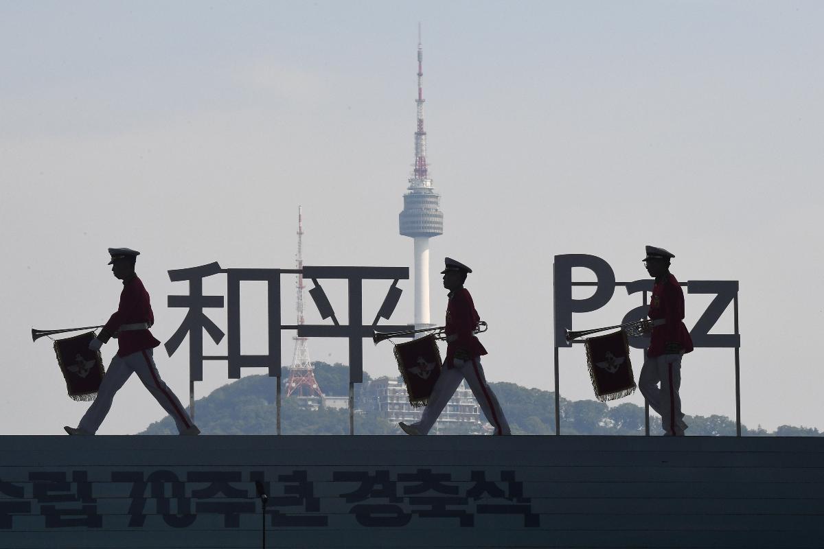 Membros da banda militar sul-coreana caminham na frente de caracteres onde se lê "Paz" durante uma cerimônia do 73º aniversário da libertação do domínio colonial japonês | JUNG YEON-JE/AFP