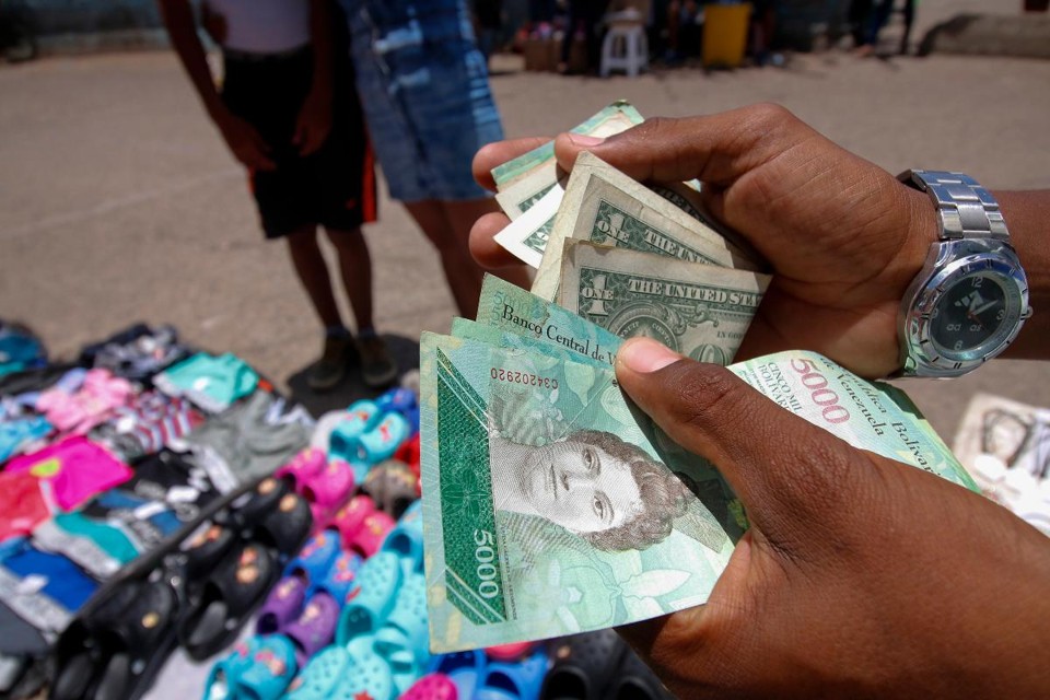 Venezuelano mostra notas de bolívar e dólar conseguidos com a venda de mercadorias na fronteira entre a Venezuela e a Colômbia | SCHNEYDER MENDOZA/AFP
