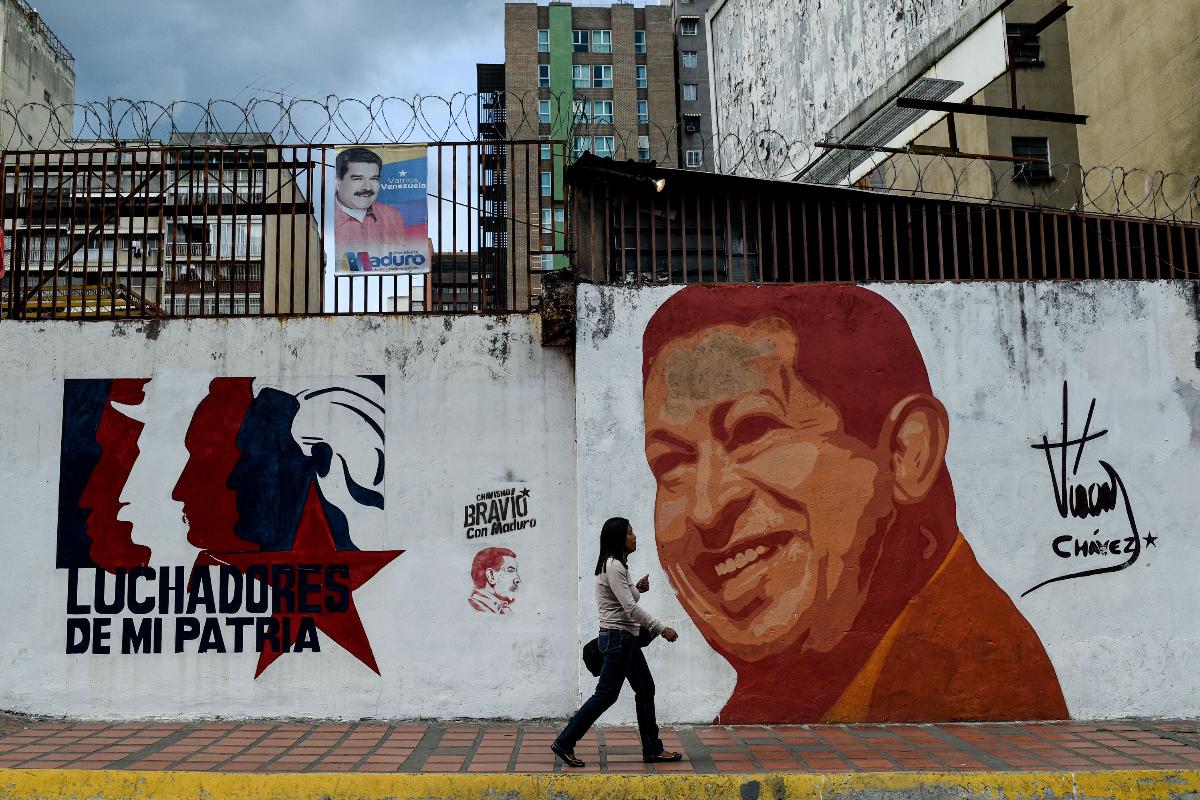 Mulher passa na frente de mural que retrata o ex-presidente venezuelano Hugo Chávez | FEDERICO PARRA/AFP