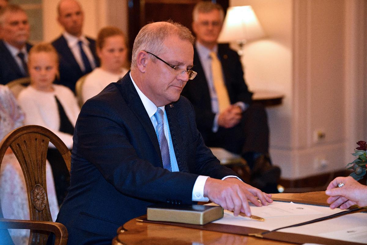 O novo primeiro-ministro australiano Scott Morrison (L) assina documentos enquanto participa de uma cerimônia de juramento em frente ao governador geral da Austrália, Peter Cosgrove, na sede do governo em Canberra, em 24 de agosto de 2018 | SAEED KHAN/AFP